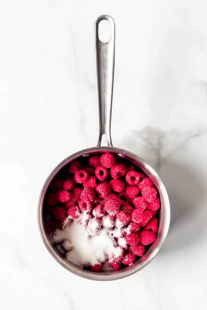 An image of frozen raspberries in a small saucepan with sugar.