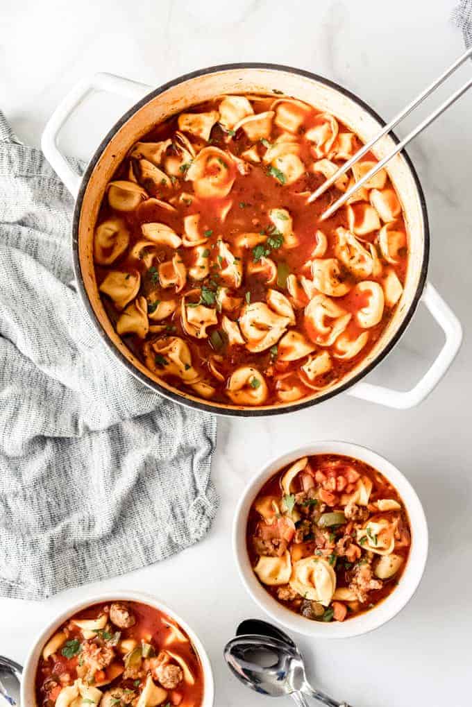 An image of a large pot of tomato basil soup with cheese tortellini and crumbled Italian sausages.