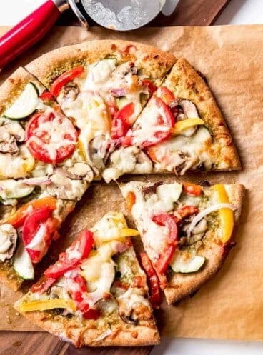 An image of a whole wheat pizza topped with fresh veggies, pesto, and cheese.