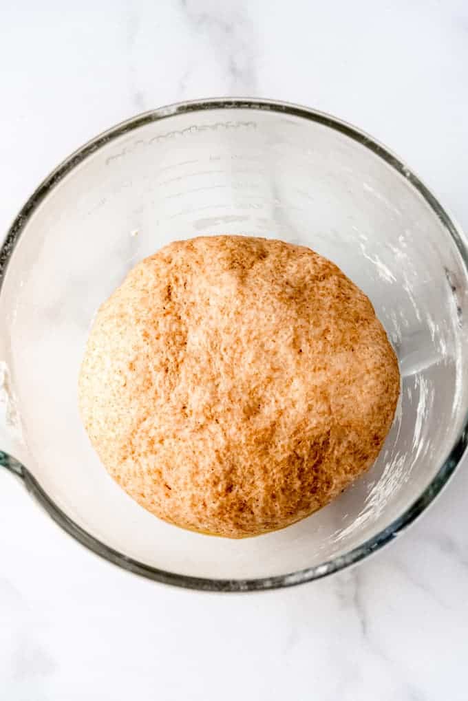 An image of whole wheat pizza dough rising in a bowl.