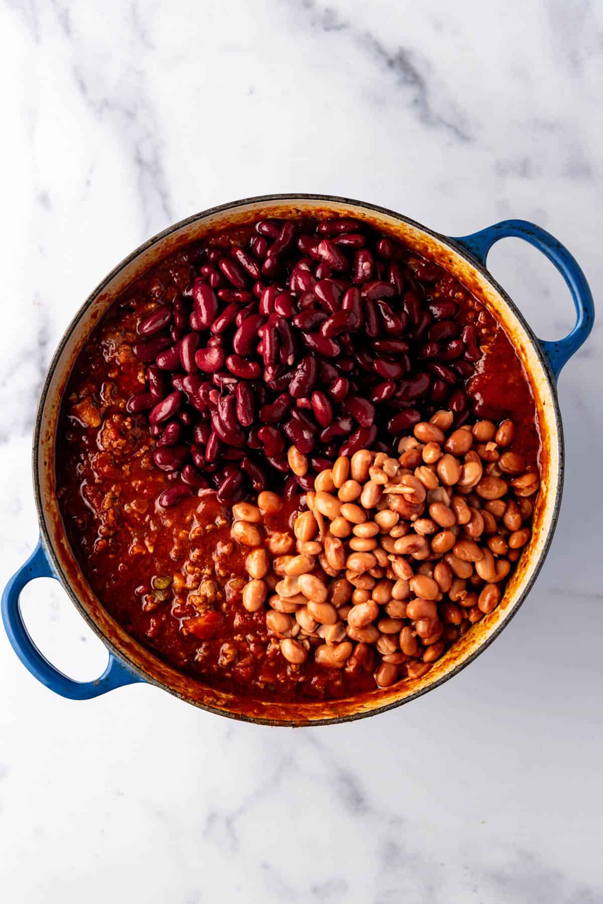 Adding two types of beans to a pot of chili.