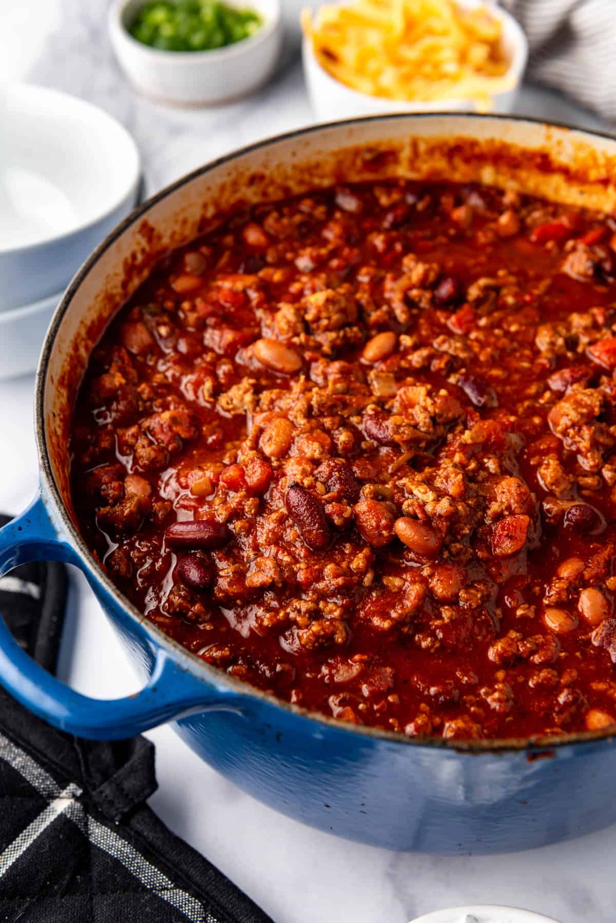 A side view of a large blue dutch oven filled with homemade chili.