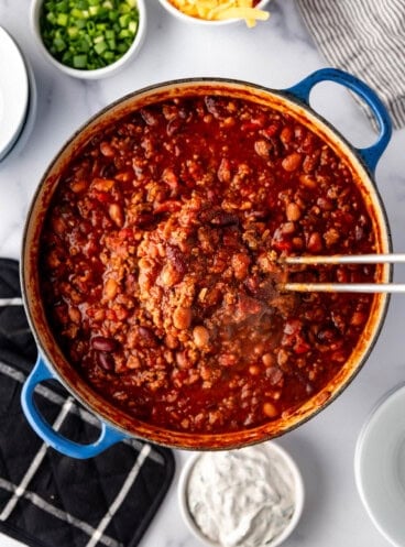 A ladleful of chili being lifted from the pot.