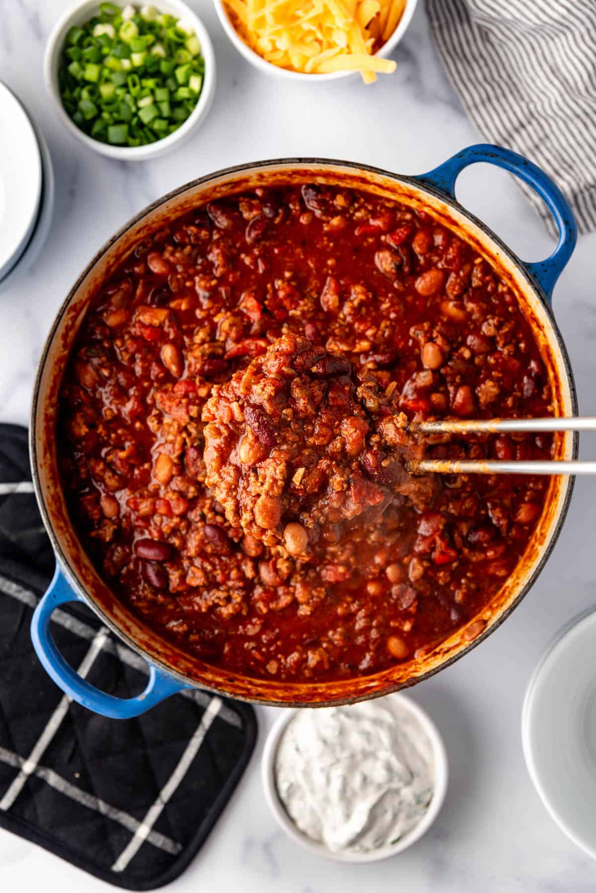 A ladleful of chili being lifted from the pot.