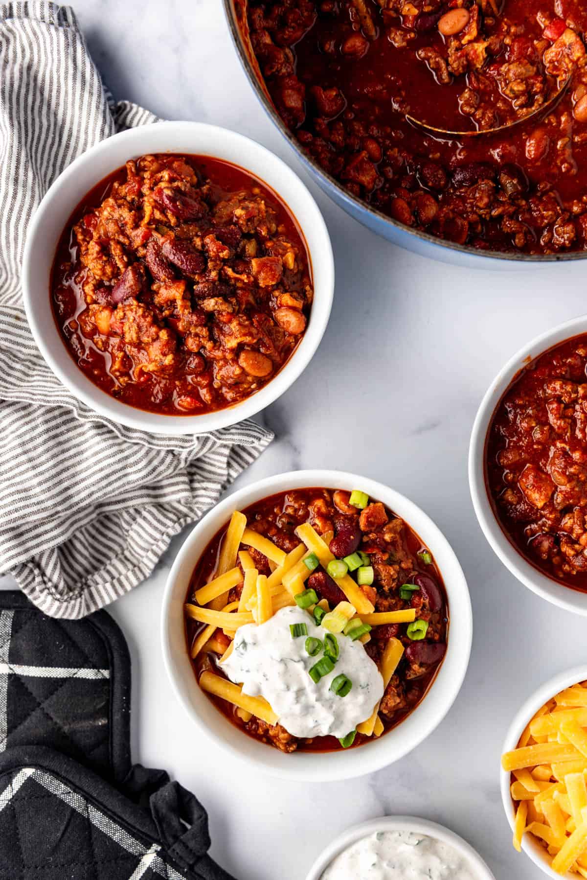 Bowls of chili topped with shredded cheese, green onions, and sour cream.