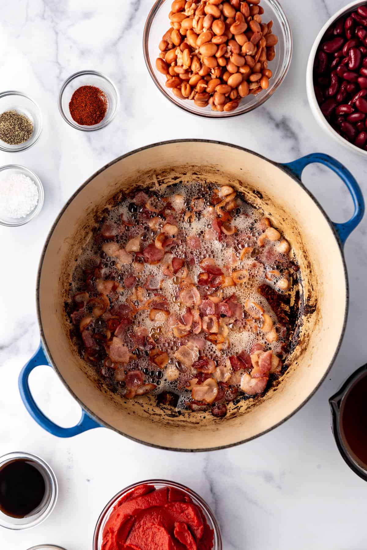 Cooking chopped bacon in a dutch oven surrounded by other chili ingredients.