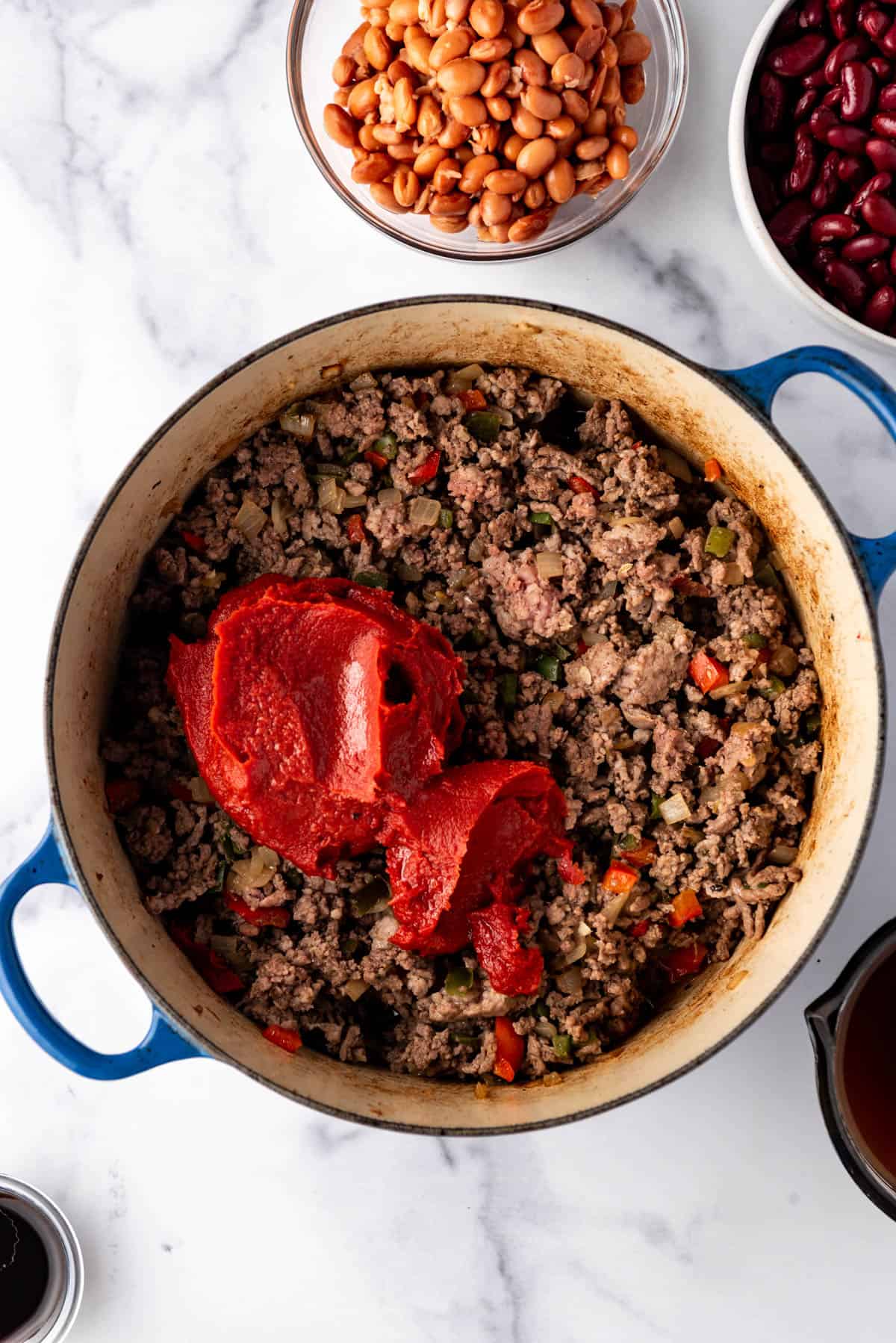 Adding tomato paste to ground meat in a large dutch oven.