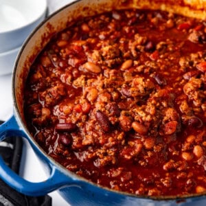 A side view of a large blue dutch oven filled with homemade chili.