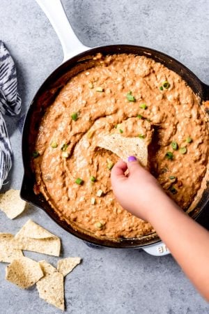 An image of a hand dipping a chip into a skillet full of bean dip