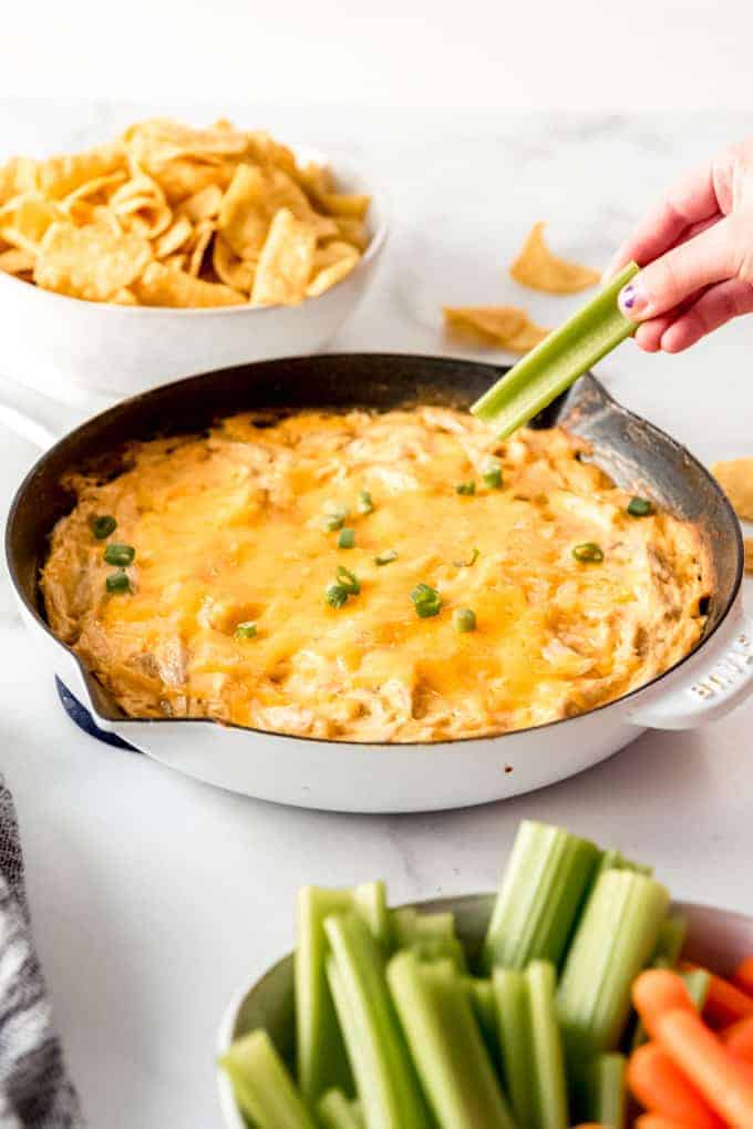 a hand dipping a celery stick into a skillet full of hot buffalo ranch chicken dip