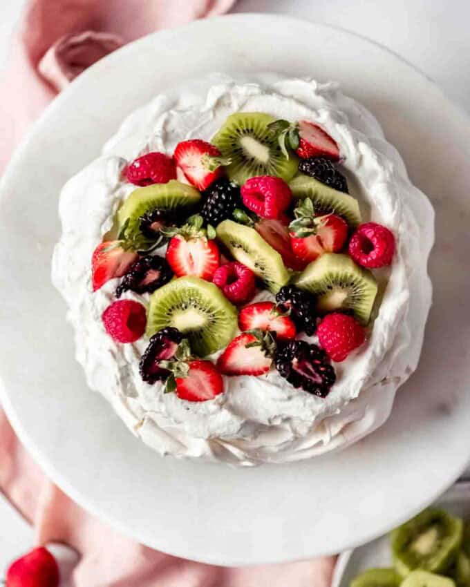 An image of sliced kiwi fruit, strawberries, blackberries, and raspberries on a New Zealand pavlova.