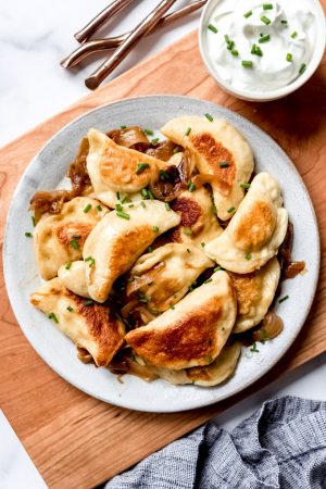 An image of homemade pierogies on a plate with chives and sour cream.