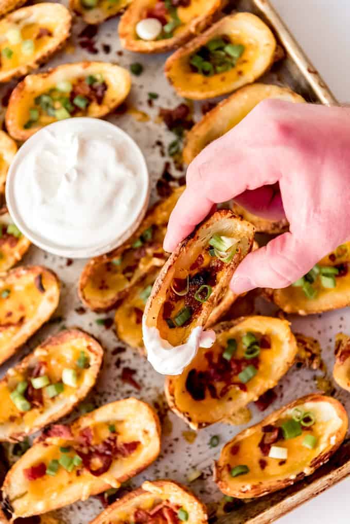 An image of a hand holding a potato skin appetizer that has been dipped in sour cream.