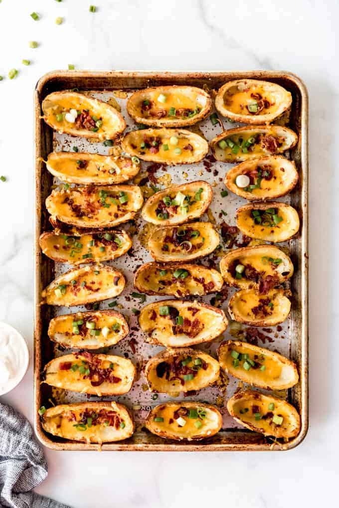 An image of a baking sheet lined with crispy potato skins topped with cheese, bacon, and green onions.