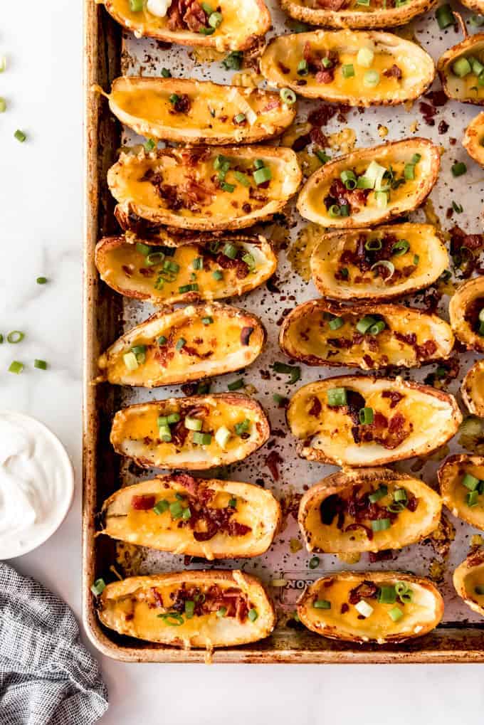 An image of cheesy potato skins with bacon on a baking sheet.