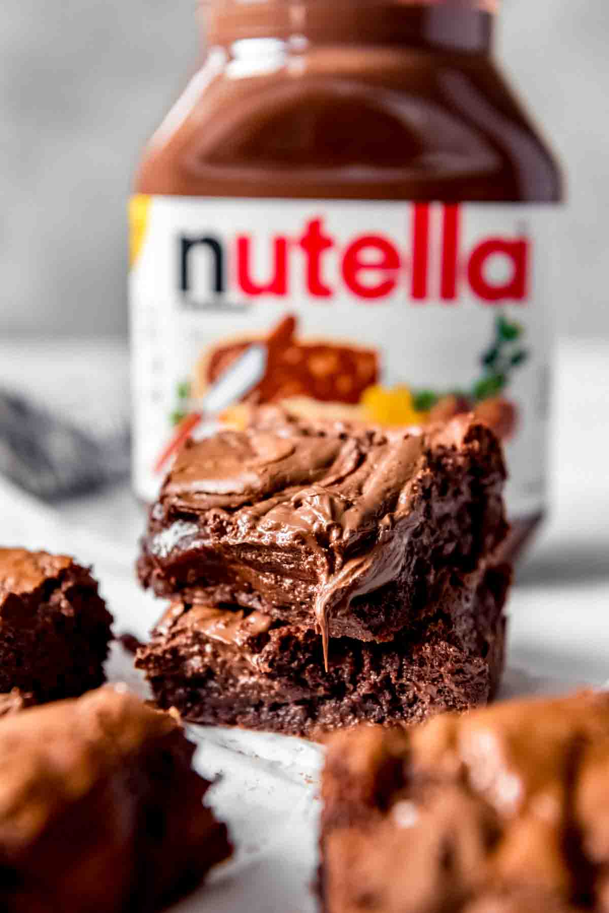 An image of gooey squares of Nutella brownies in front of a jar of Nutella.