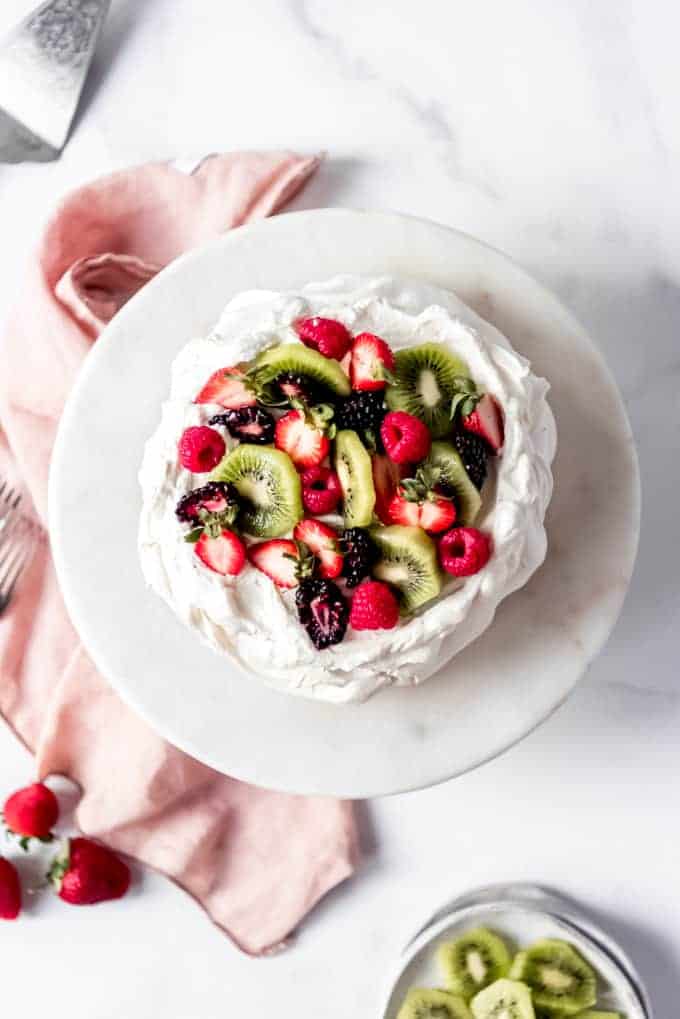 An image of a pavlova cake topped with fresh kiwi, strawberries, and blackberries.
