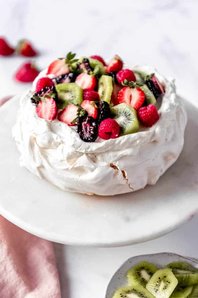 An image of a large pavlova dessert topped with fresh cream and fruit.