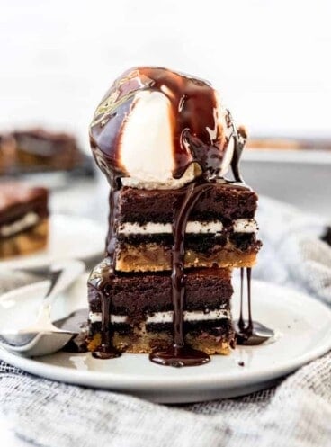 Two slutty brownies stacked on a plate with a scoop of vanilla ice cream on top.