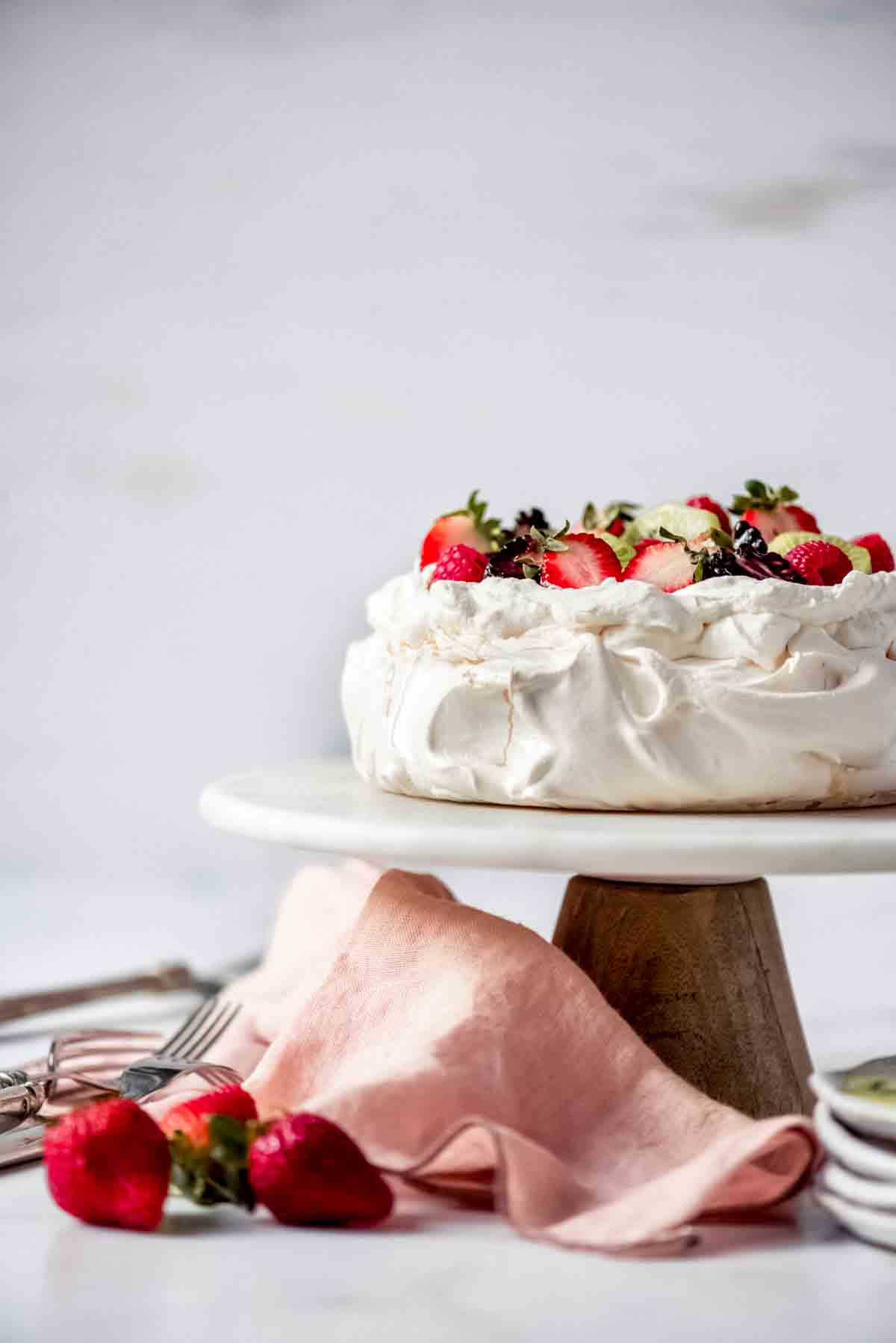 An image of a cake stand with a meringue dessert topped with cream and fresh fruit.