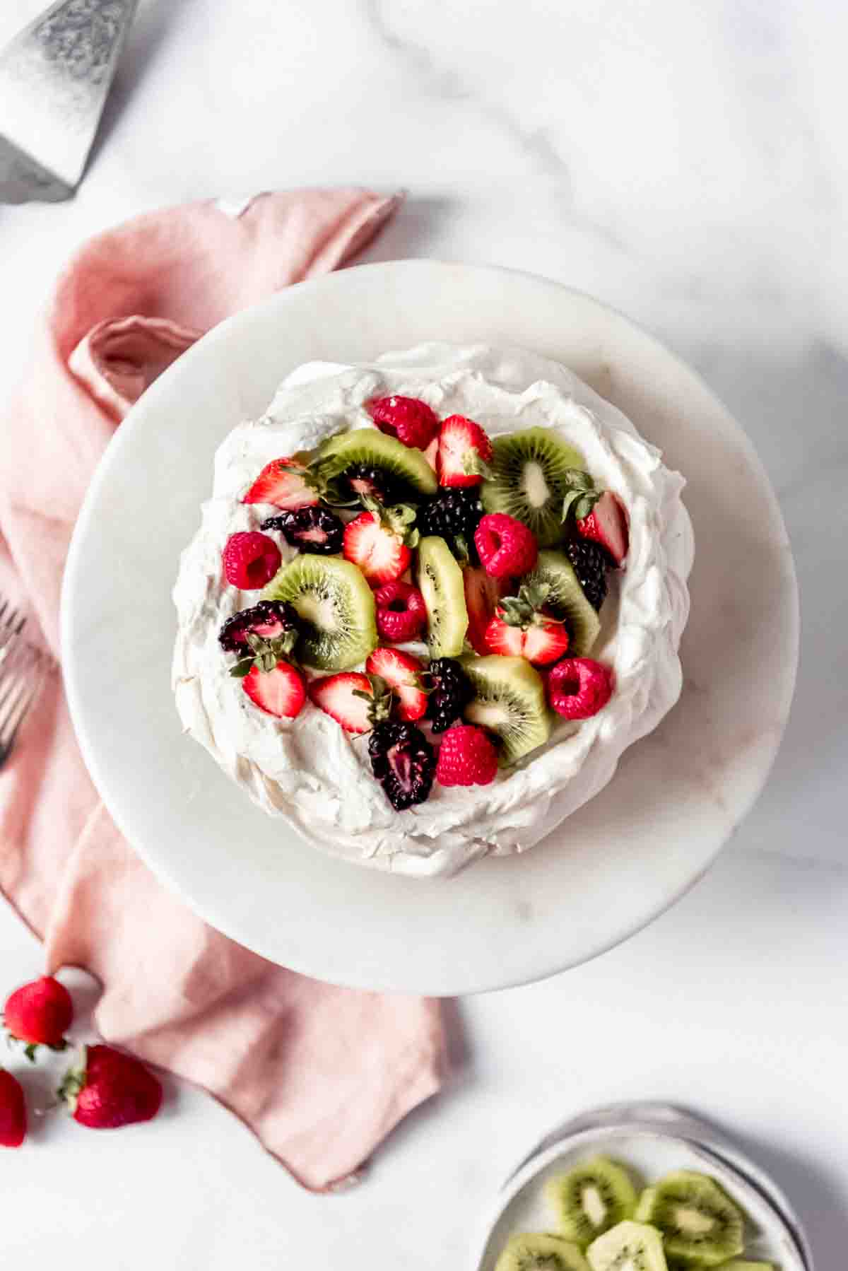 An image of a pavlova cake topped with fresh kiwi, strawberries, and blackberries.