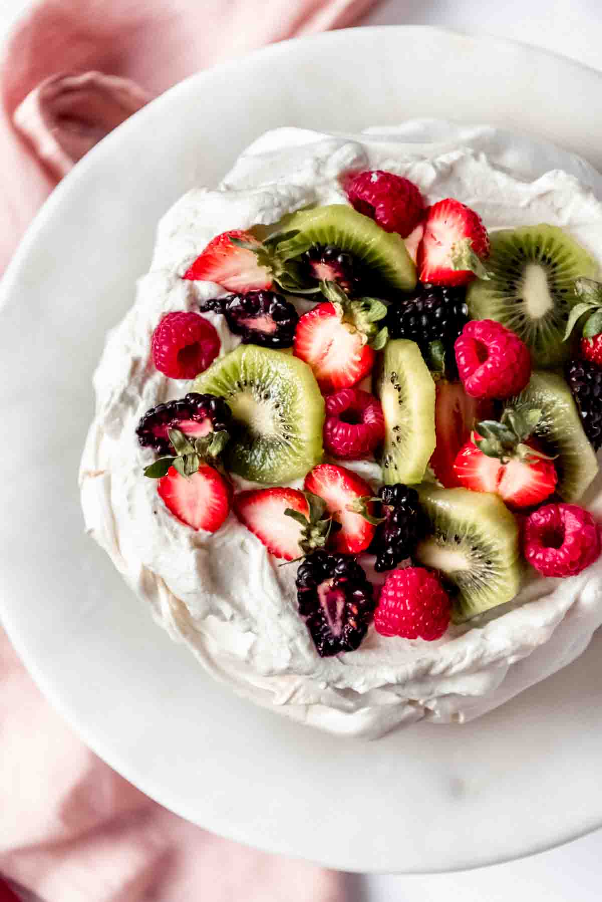 An image of sliced kiwi fruit, strawberries, blackberries, and raspberries on a New Zealand pavlova.