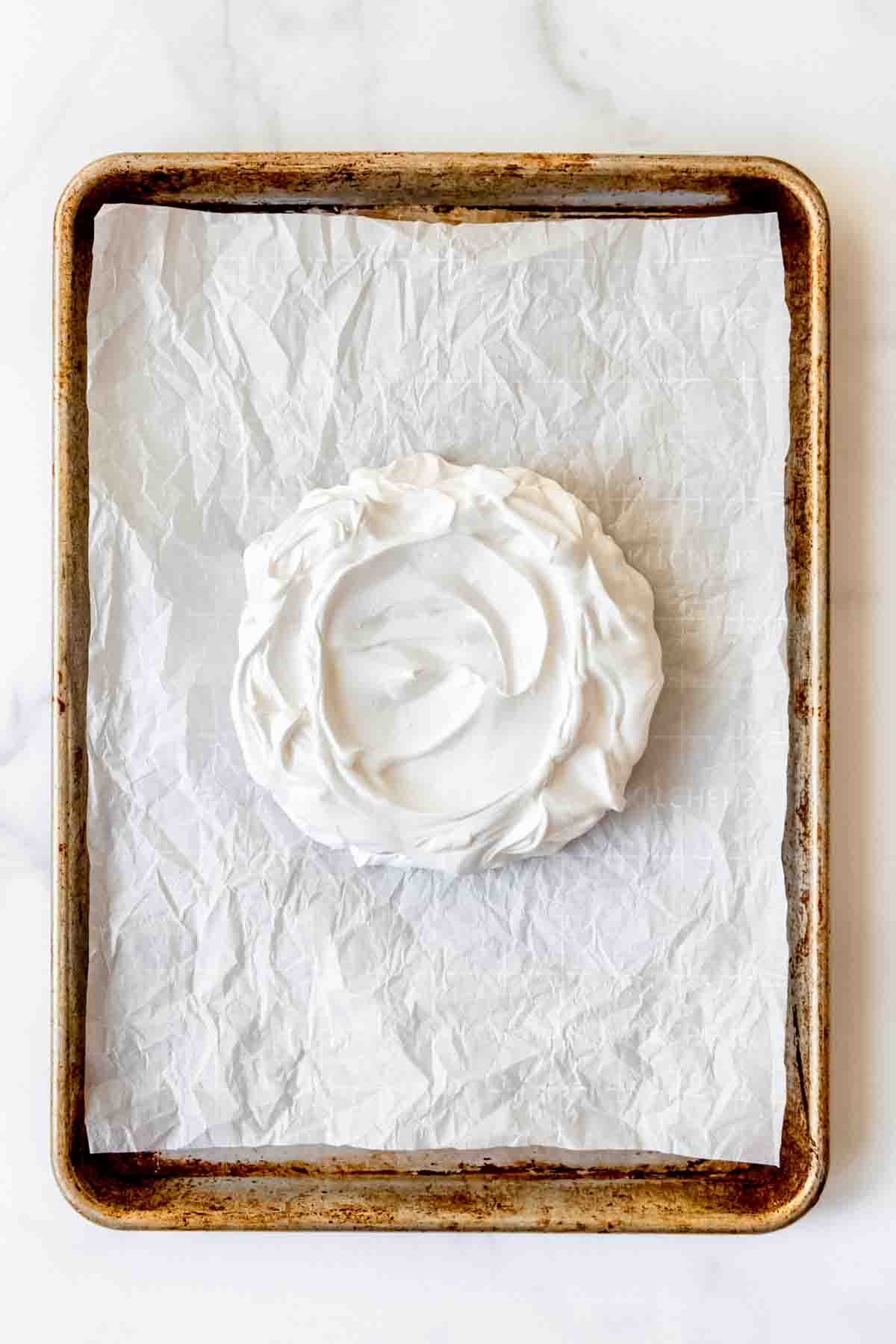 Whipped meringue on a piece of parchment paper on a baking sheet.