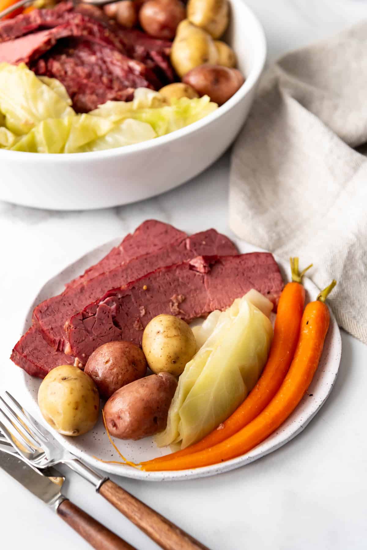 Slices of corned beef on a plate with cabbage, carrots, and potatoes.