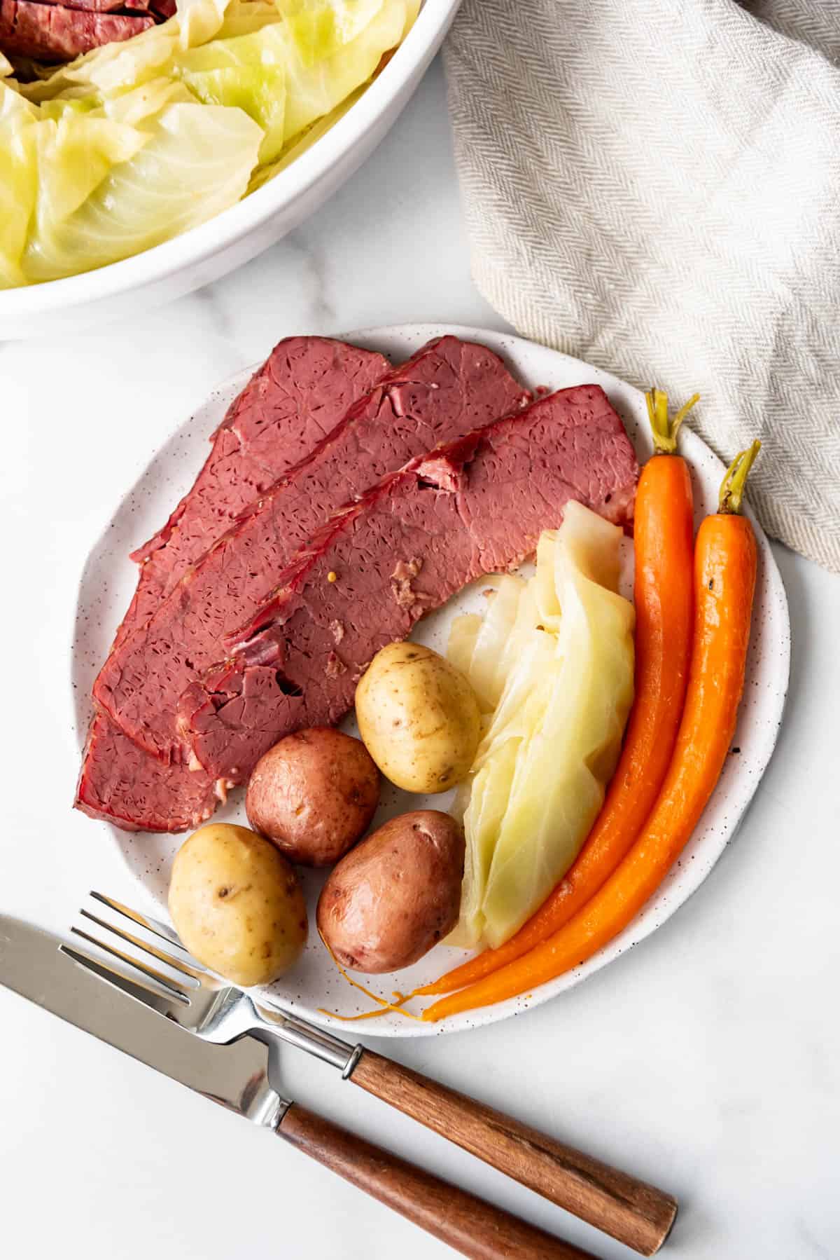 An image of a plate of slices of corned beef and cabbage with boiled potatoes and carrots.