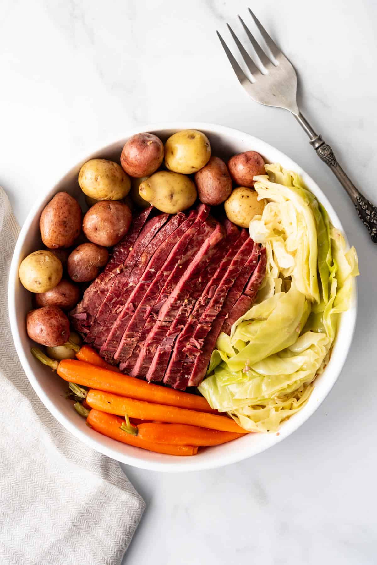 An overhead image of a bowl of corned beef, cabbage, boiled potatoes, and carrots.