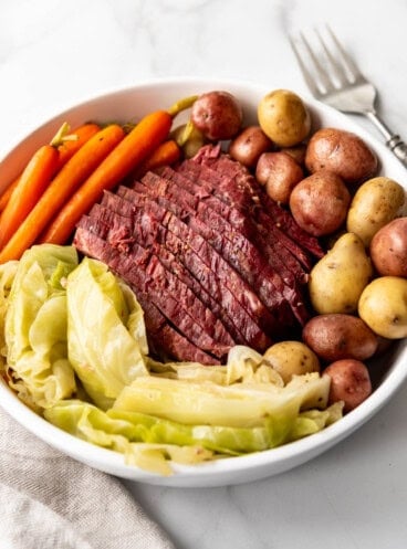 An image of a sliced corned beef brisket served on a platter with boiled potatoes, cooked cabbage, and carrots.