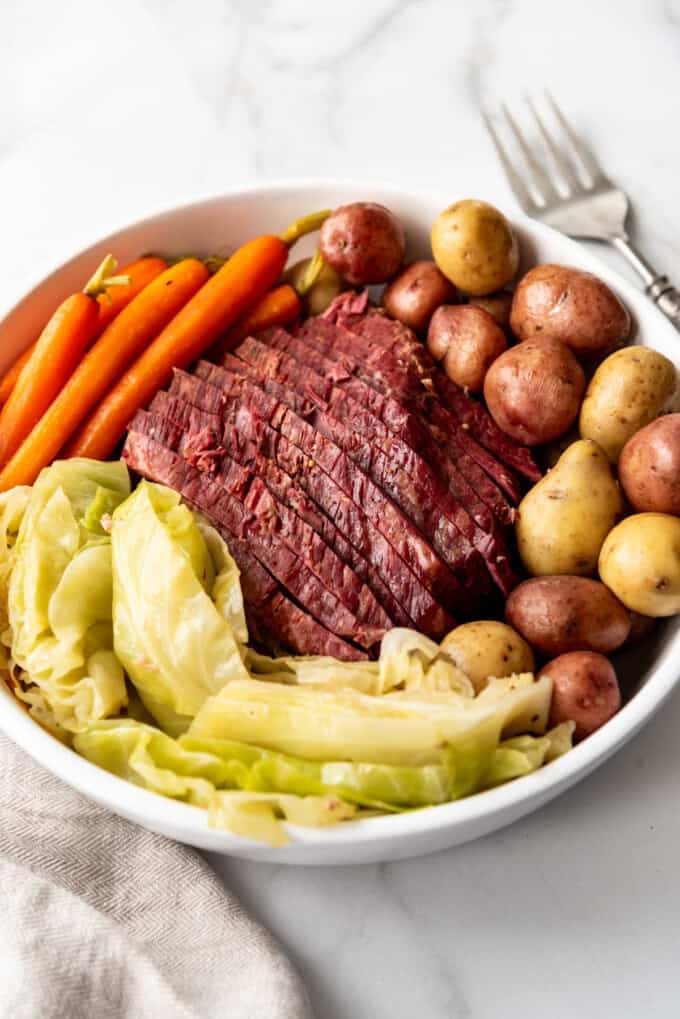 An image of a sliced corned beef brisket served on a platter with boiled potatoes, cooked cabbage, and carrots.