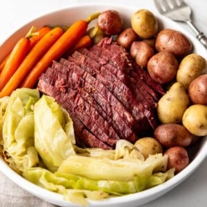 An image of a sliced corned beef brisket served on a platter with boiled potatoes, cooked cabbage, and carrots.