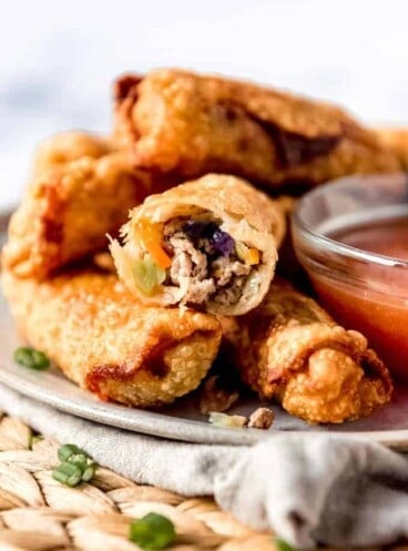 a plate full of crispy eggrolls and a bowl of dipping sauce