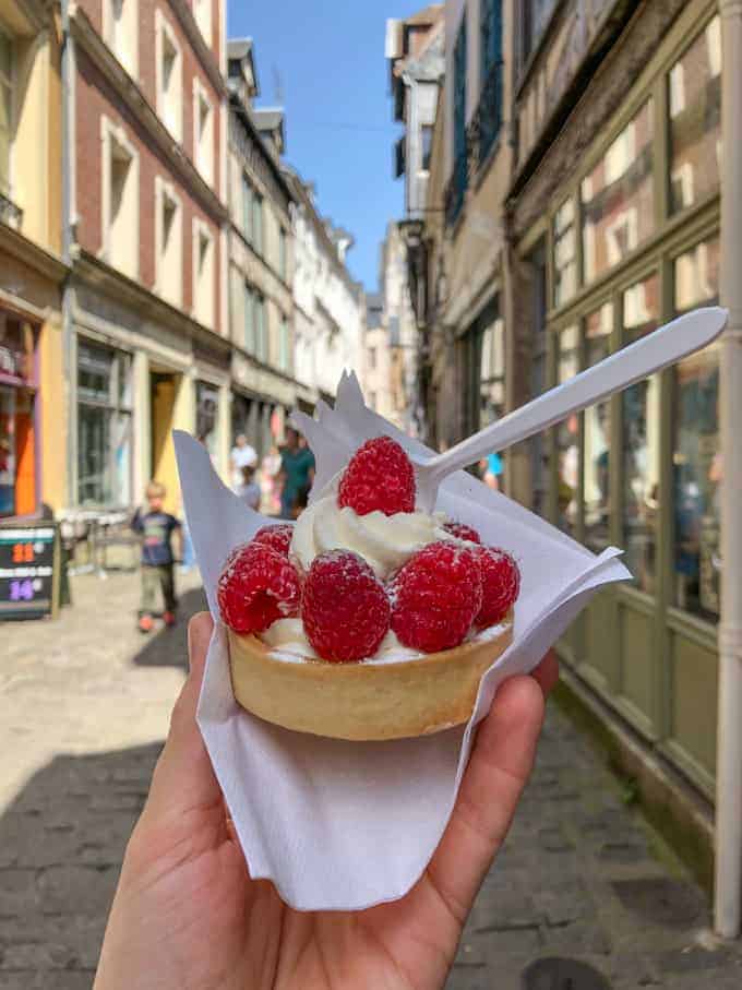 An image of a hand holding a French raspberry tartlet.