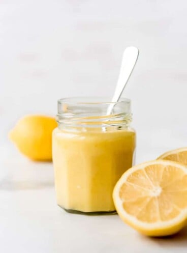 An image of a jar of homemade lemon curd with sliced lemons to the sides