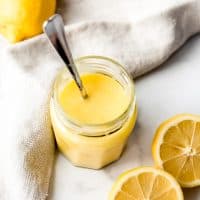 An image of easy homemade lemon curd in a jar next to fresh lemons.