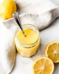 An image of easy homemade lemon curd in a jar next to fresh lemons.