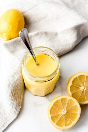 An image of easy homemade lemon curd in a jar next to fresh lemons.