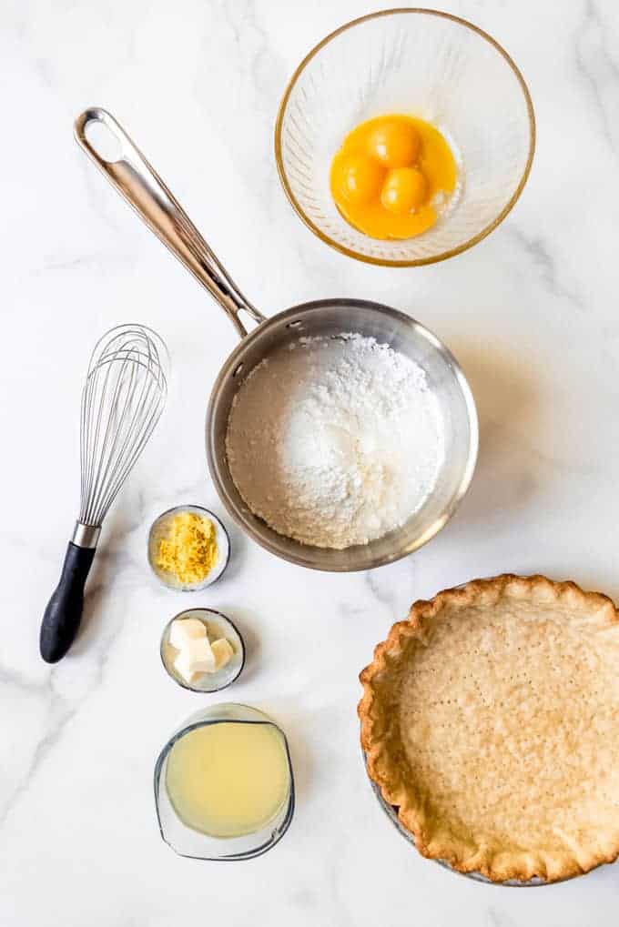 All the ingredients for lemon meringue pie laid out on a marble surface.