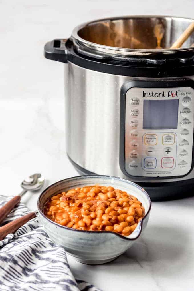 An image of a bowl of homemade pork and beans next to an electric pressure cooker.