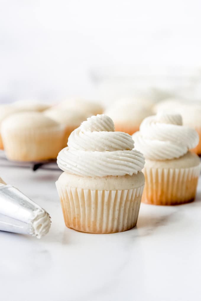 An image of vanilla buttercream frosting piped in swirls onto white cupcakes.