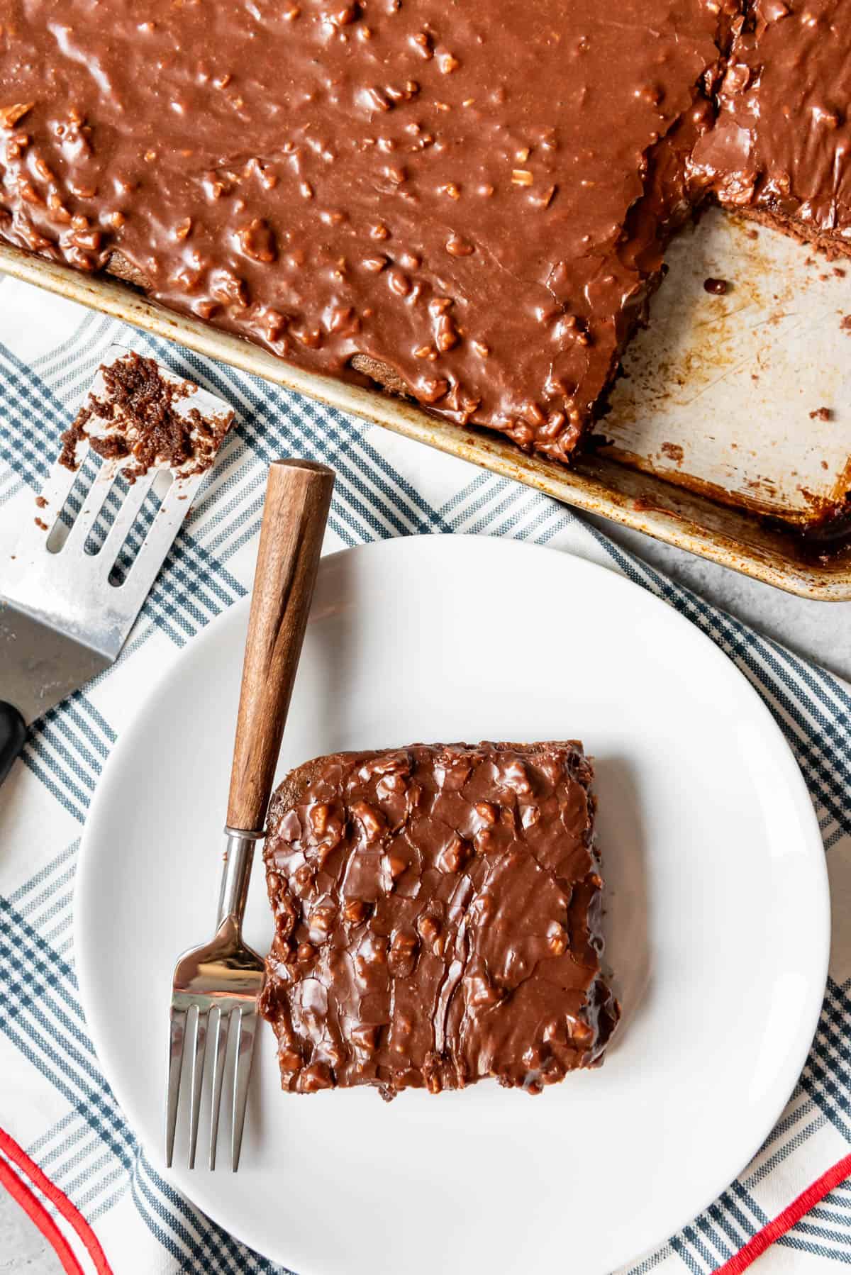 An image of a slice of Texas sheet cake with pecans next to a sheet pan.