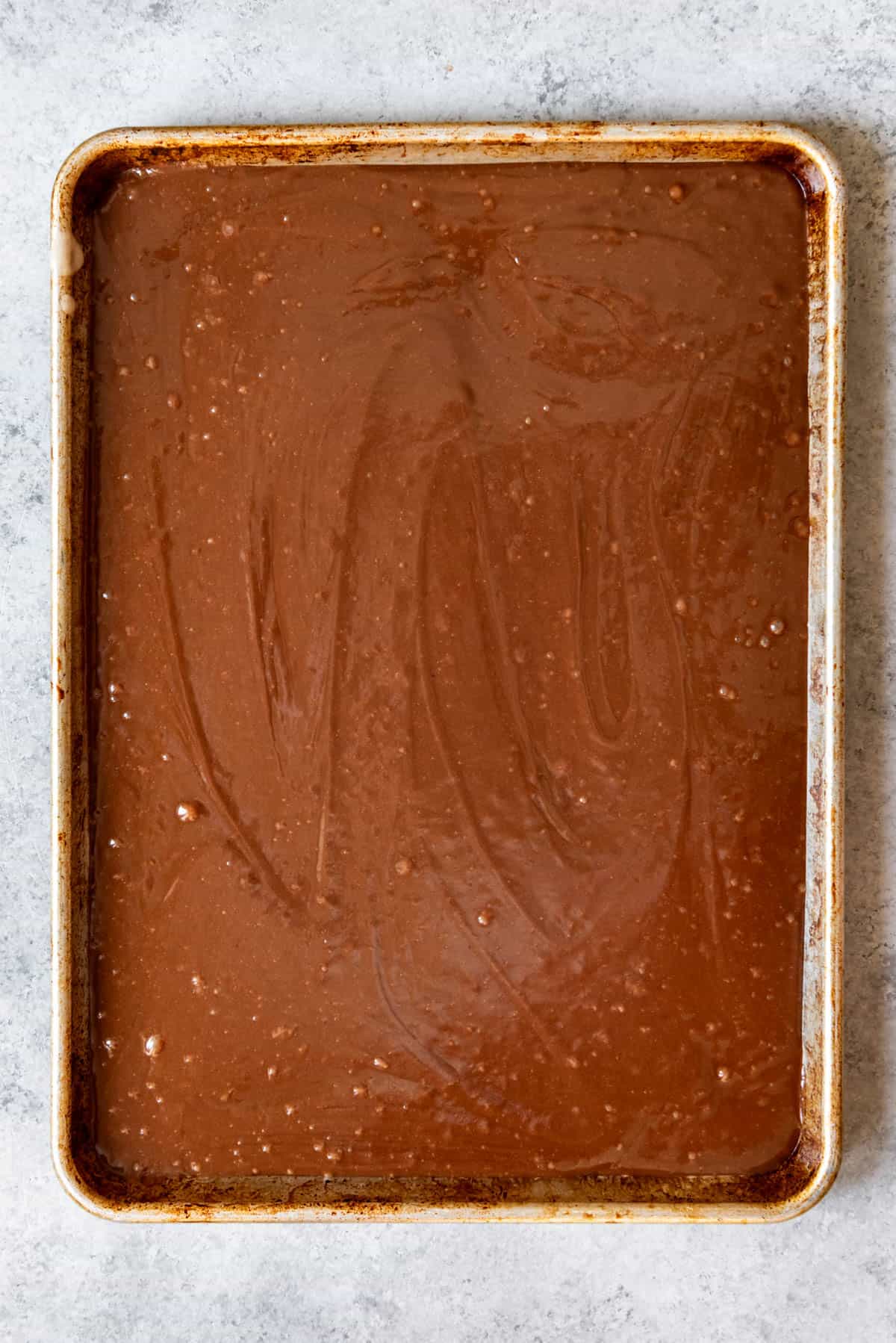 An image of chocolate cake batter poured into a baker's half-sheet pan.