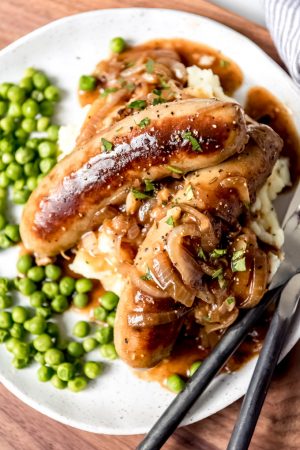 An image of British bangers and mash with onion gravy and peas.
