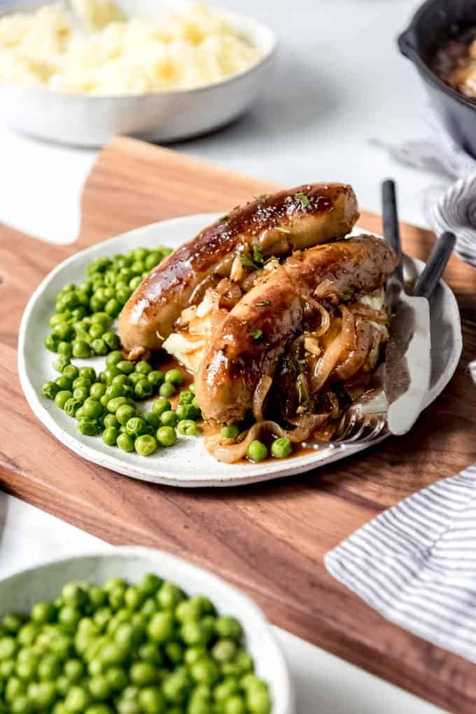An image of cooked Irish banger sausages on top of mashed potatoes with peas.