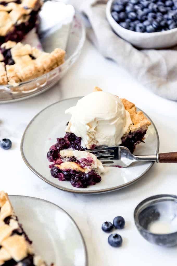 A piece of homemade blueberry pie with ice cream on a plate.