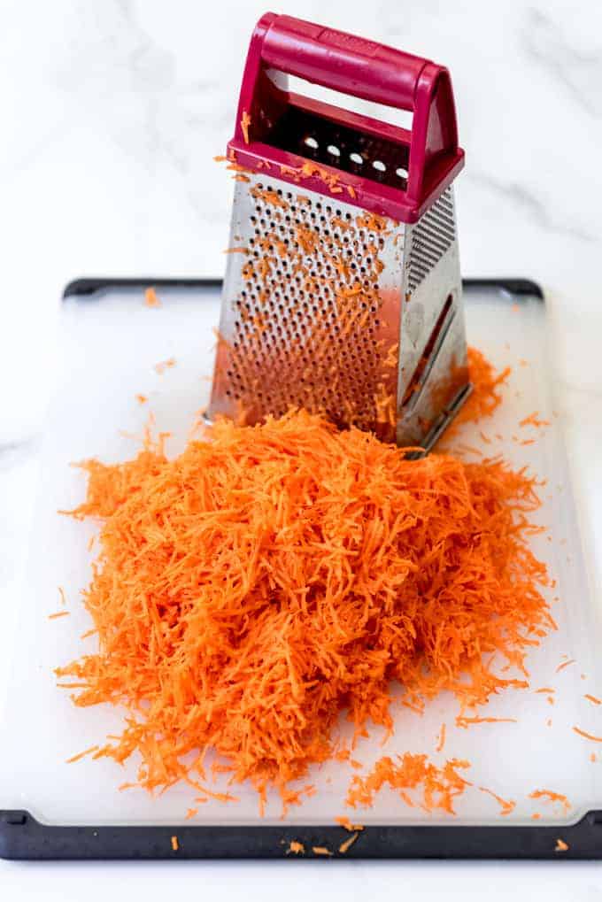 An image of finely shredded carrots in front of a box grater.
