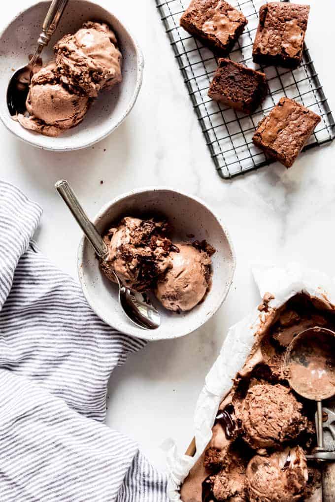 Bowls filled with scoops of chocolate ice cream next to brownies on a wire rack.