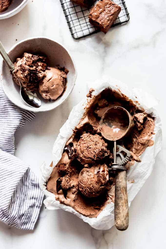 Scoops of chocolate ice cream with a vintage scoop in a pan of homemade ice cream next to a bowl of more ice cream.